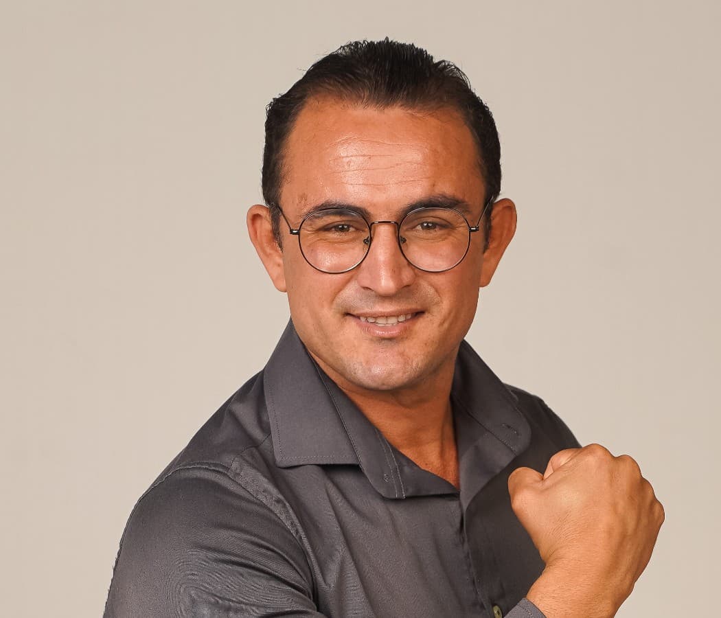 Retrato de Romário Leal usando camisa cinza e óculos.